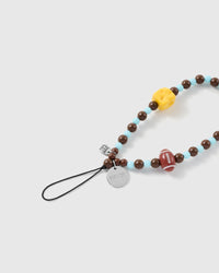 Close-up of the black stretch-cord loop and silver engraved STICKYZOO disc beside a yellow cheese bead and maroon football on brown and blue beads.