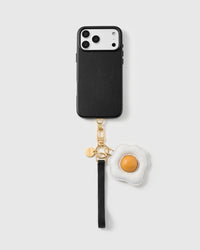 Leather fried-egg phone strap clipped to a black phone case, worn hands-free from the wrist