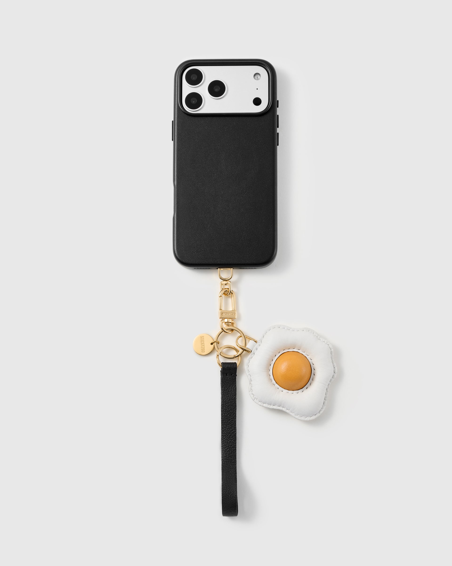 Leather fried-egg phone strap clipped to a black phone case, worn hands-free from the wrist