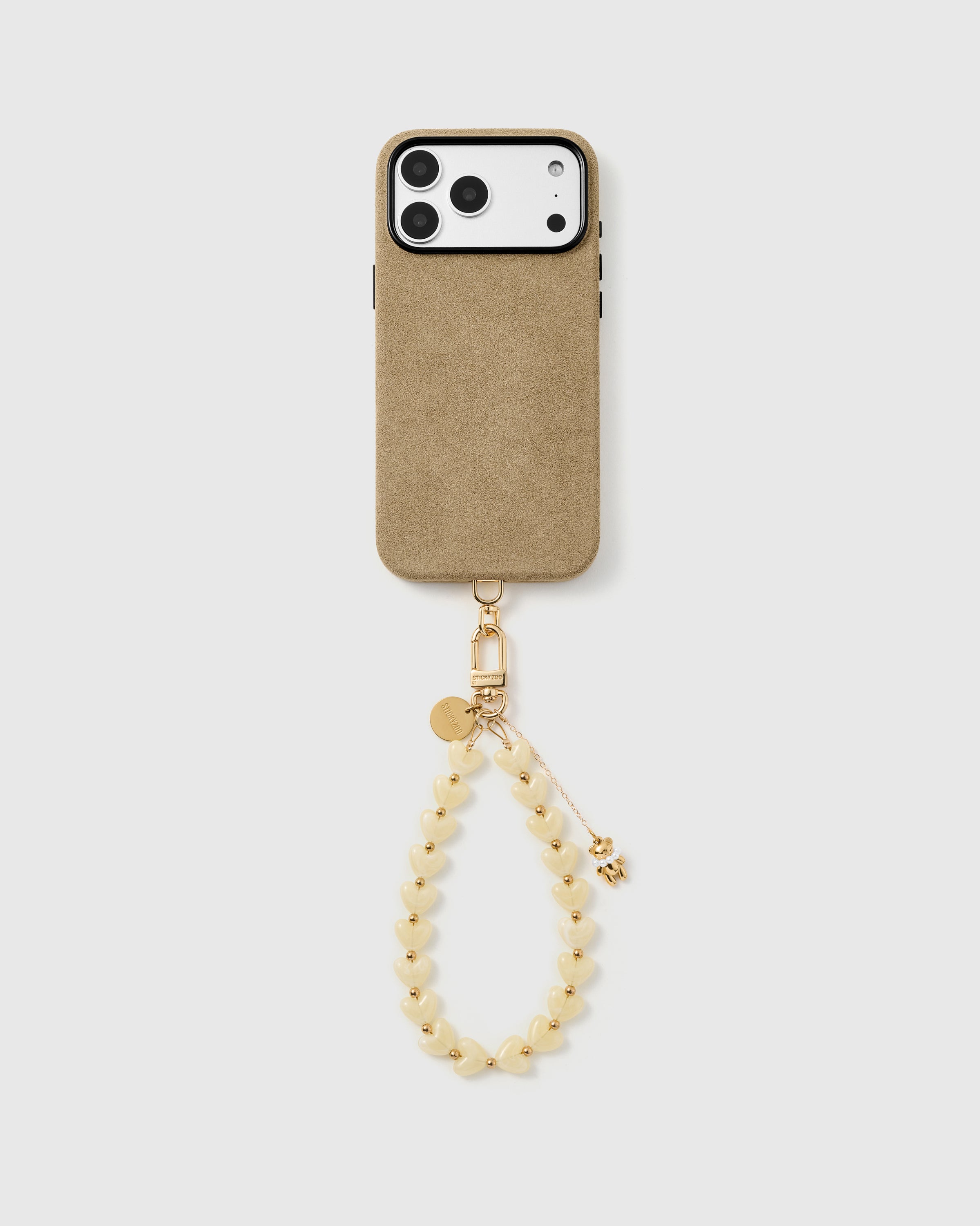 Full phone with the ivory teddy heart strap clipped on, hanging from the base of a black phone case.