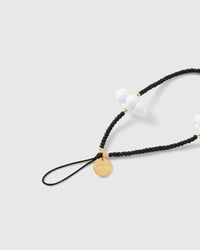 Close-up of the gold-tone STICKYZOO disc and black stretch-cord loop, with matte black beads, gold accents and a white cloud cluster.