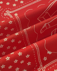 Silk scarf folds catching light against the crimson field and the cream printed motif
```