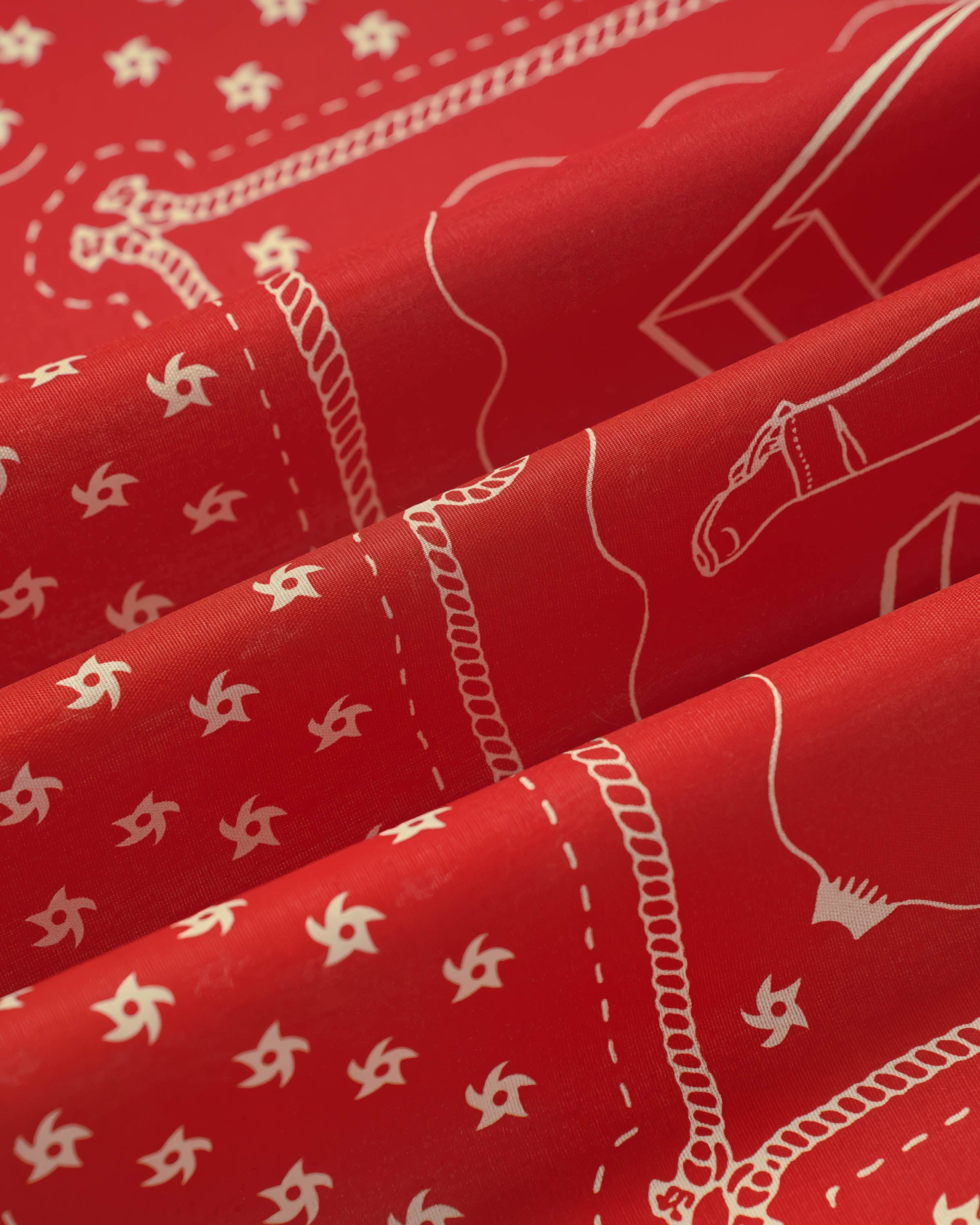 Silk scarf folds catching light against the crimson field and the cream printed motif
```