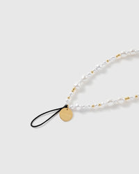 Close-up of the black stretch-cord loop and engraved gold-tone STICKYZOO disc, with glossy baroque faux-pearls and gold ball beads.