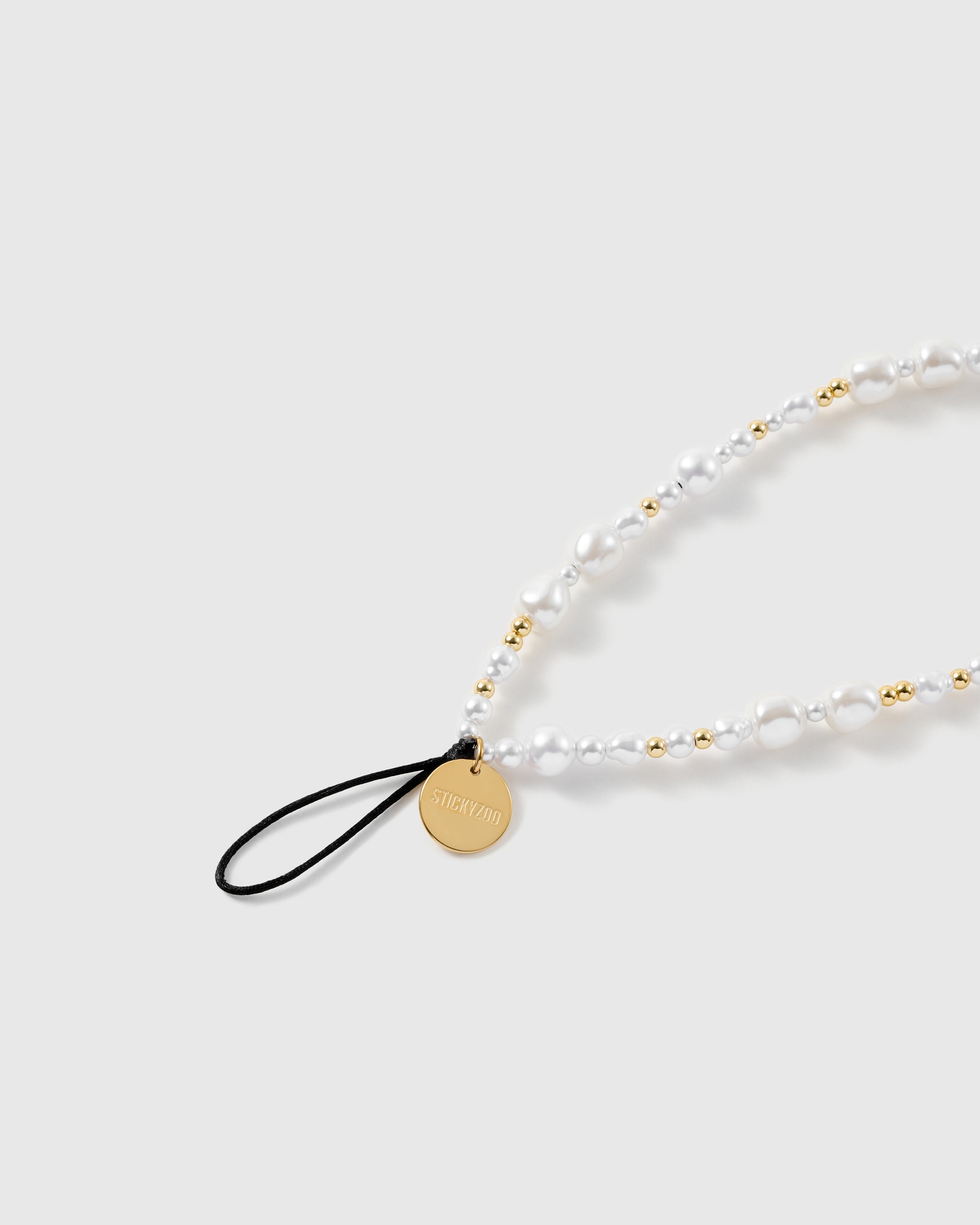 Close-up of the black stretch-cord loop and engraved gold-tone STICKYZOO disc, with glossy baroque faux-pearls and gold ball beads.