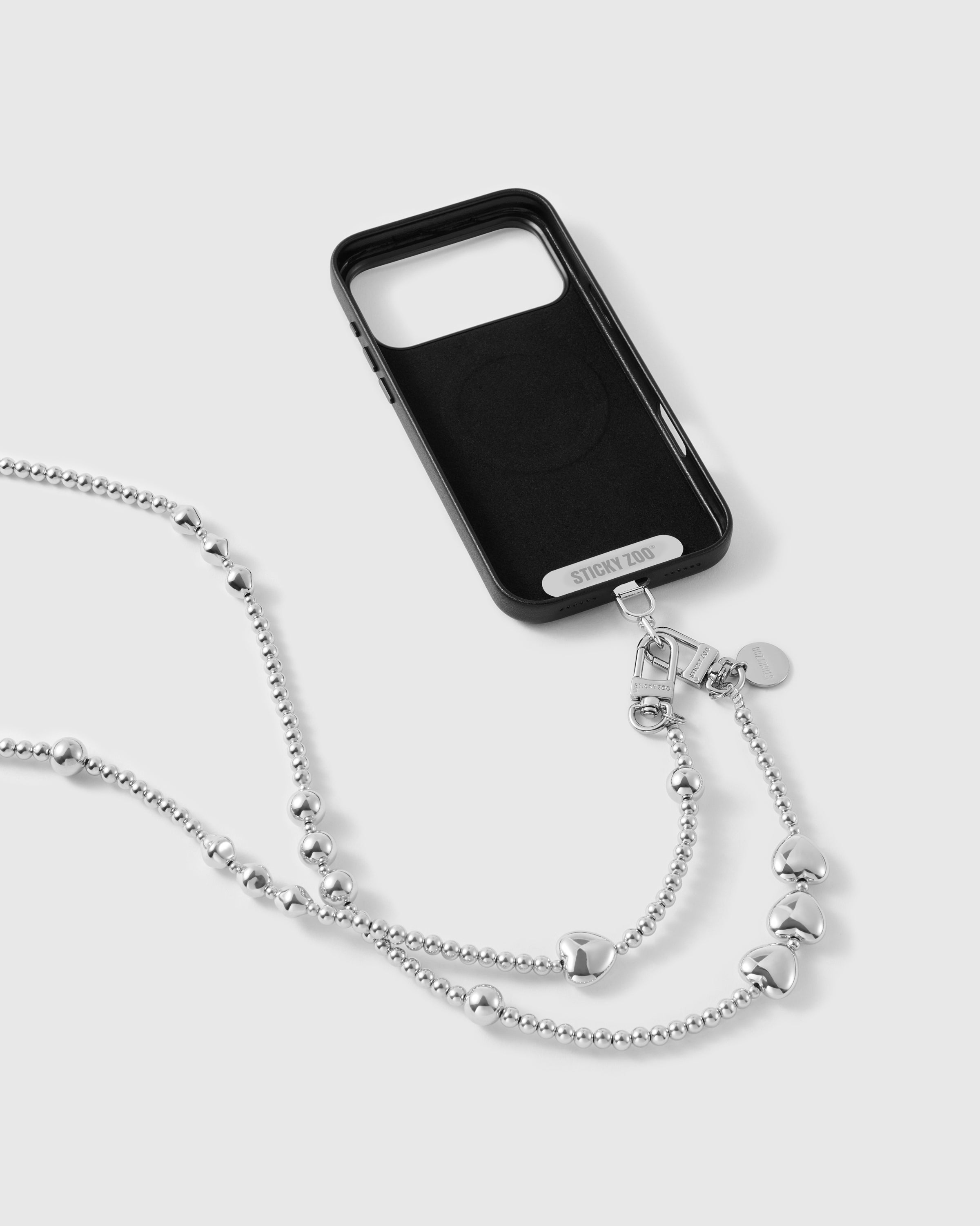 Black phone case marked STICKYZOO with the silver-tone strap clipped on by dual clasps, ball-bead chain and puffy hearts draping below.