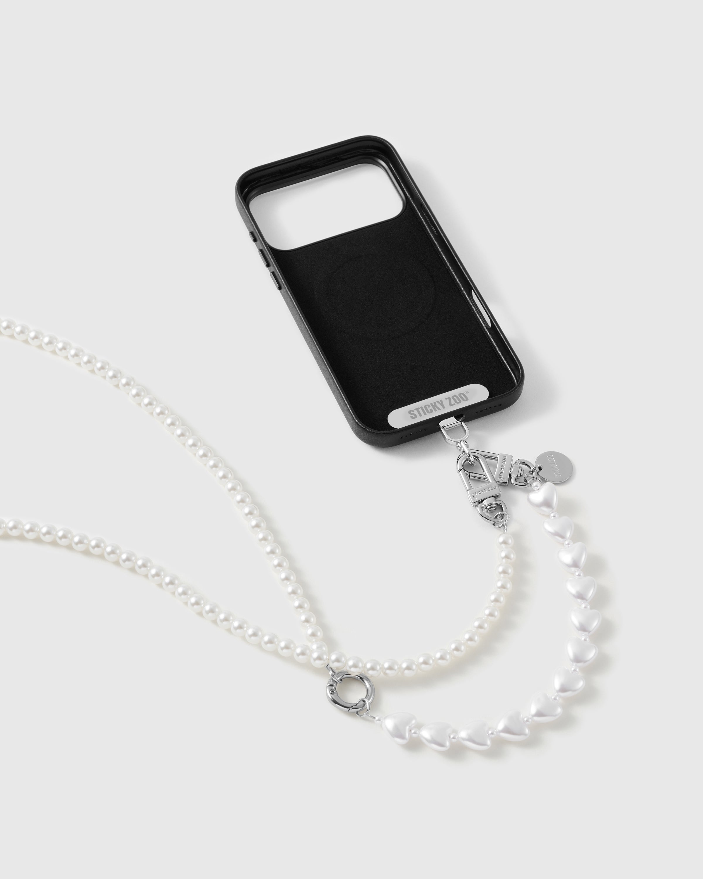 Black phone case marked STICKYZOO with the pearl-and-heart strap clipped on, silver-tone clasp, disc charm and O-ring visible.