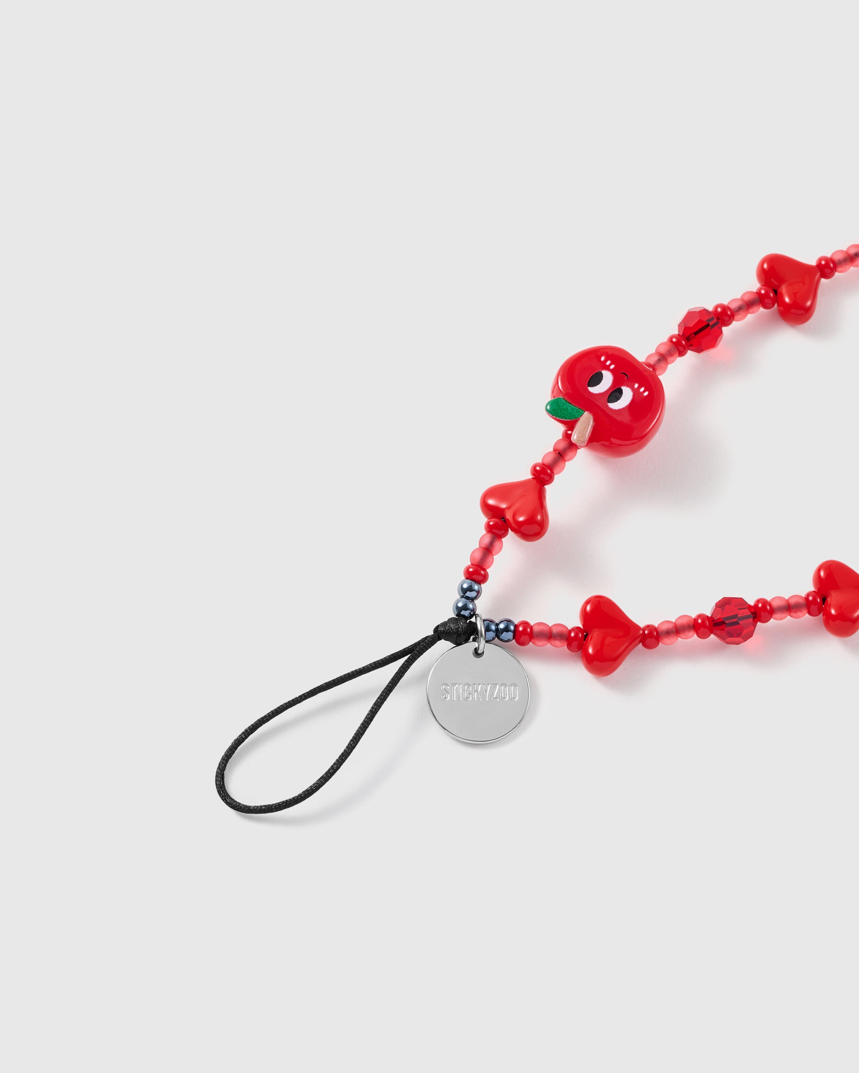 Close-up of the smiley apple charm, faceted red beads and glossy puff hearts on a handmade phone strap