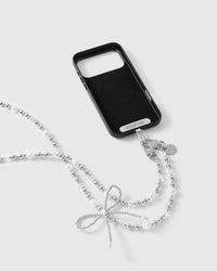 Black-cased phone clipped to the strap by dual silver-tone clasps, the woven silver-tone bow resting in front on a light background.