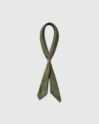 STICKYZOO clover stirrup silk scarf looped with a leather slide showing the scattered green stirrup motif