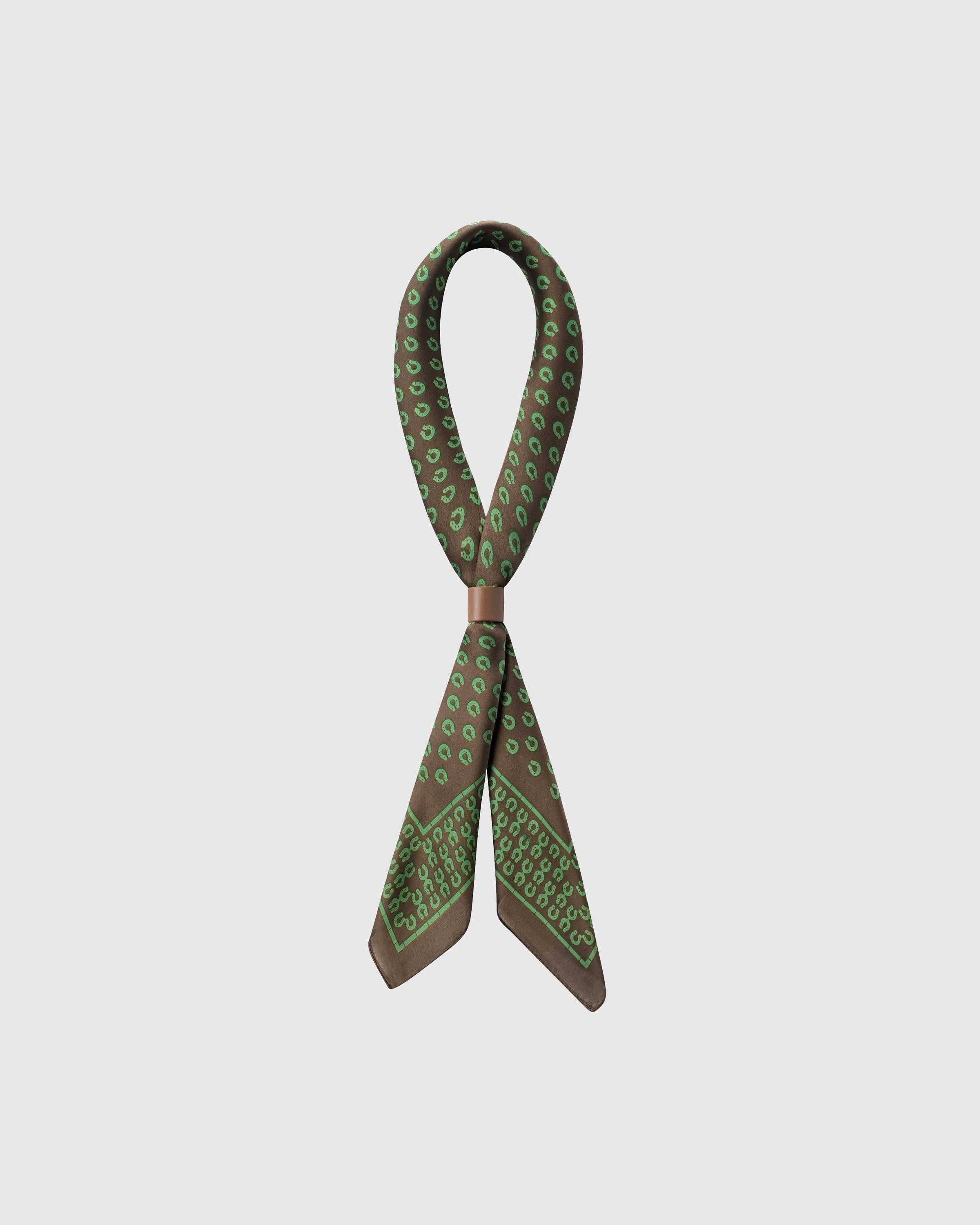 STICKYZOO clover stirrup silk scarf looped with a leather slide showing the scattered green stirrup motif