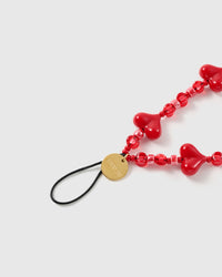 Close-up of translucent cherry beads, glossy puff hearts and pink accent beads on a handmade phone strap
