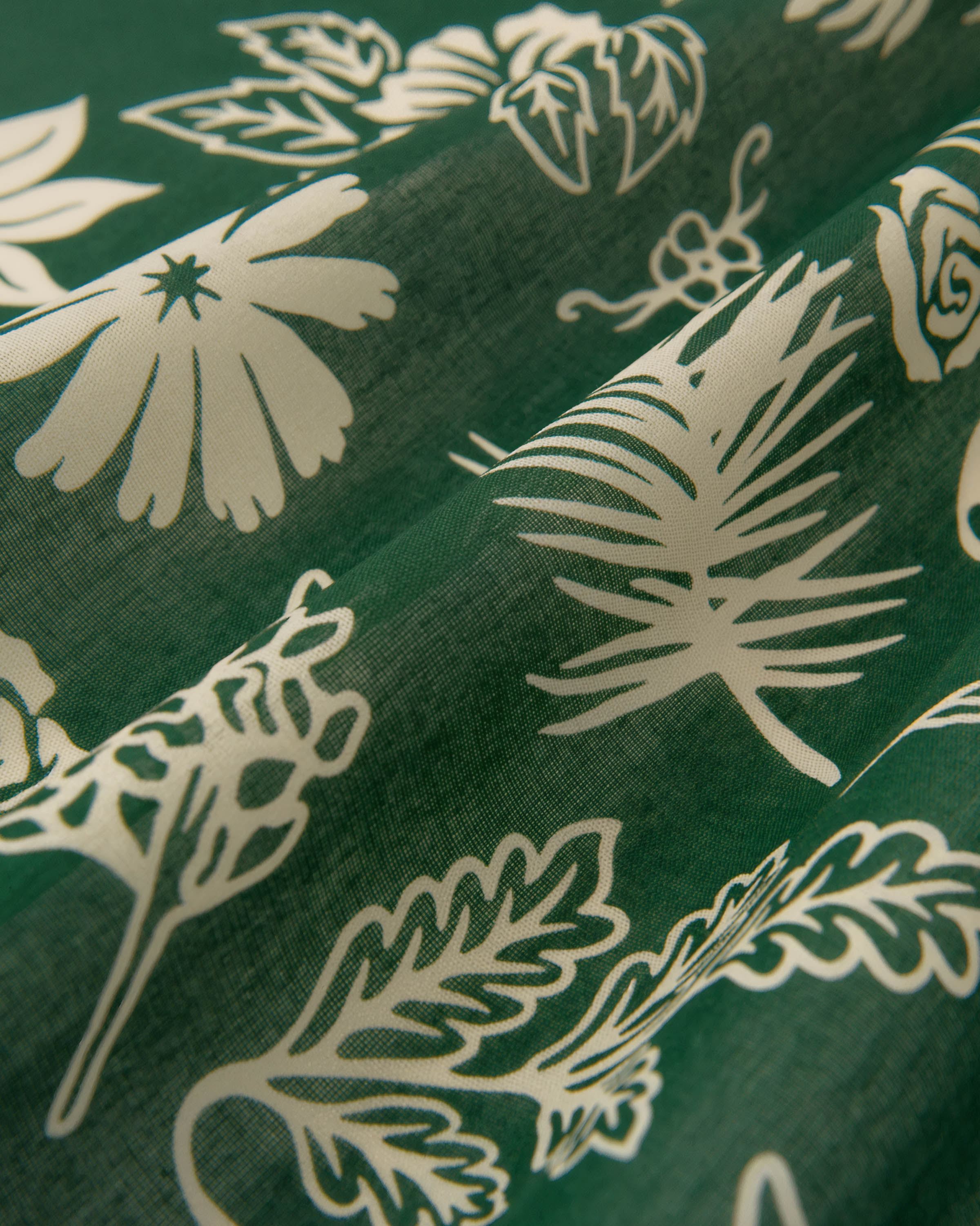 Close-up of hand-illustrated daisies, palms and ferns printed in ivory on the forest-green silk field
```