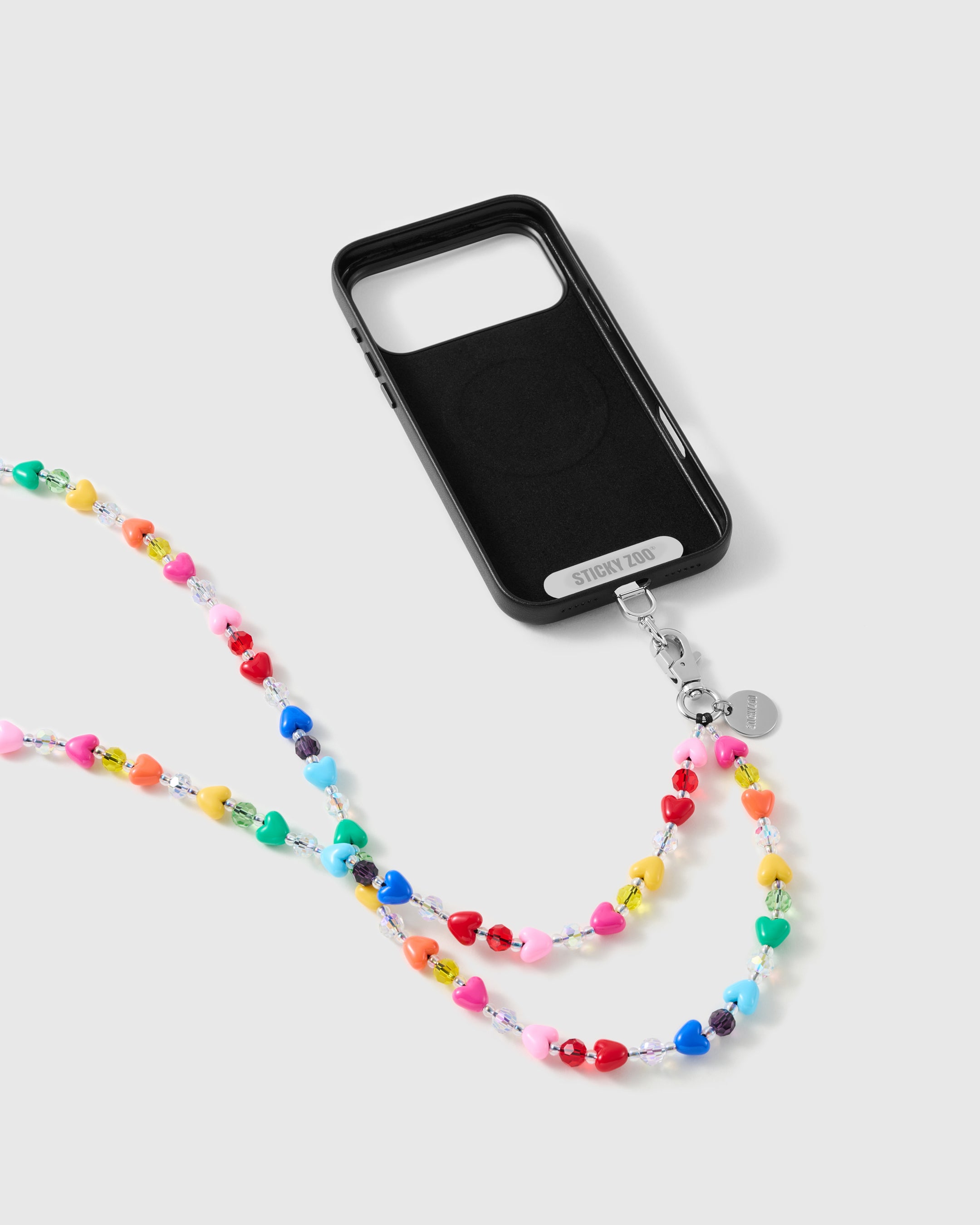 Rainbow heart-bead strap clipped to a black phone case with a silver-tone clasp and STICKYZOO connector tab, ready to wear cross-body.