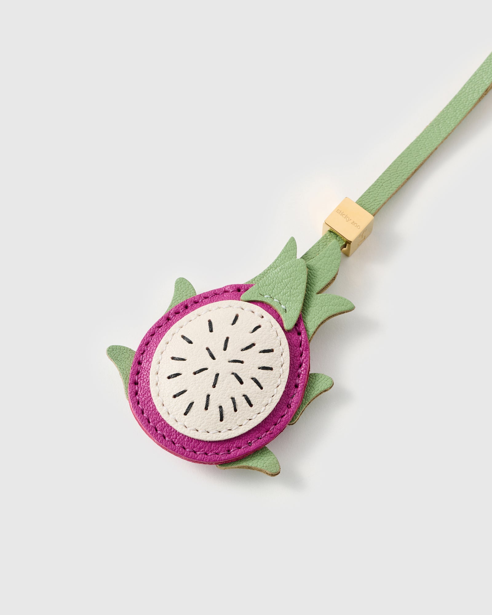 Close-up of layered French Alran leather pitaya charm showing hand-stitched black seeds across cream flesh face and magenta border