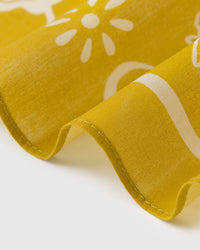 Close-up of the mustard silk scarf coiled to show the soft drape and ivory daisy silhouette