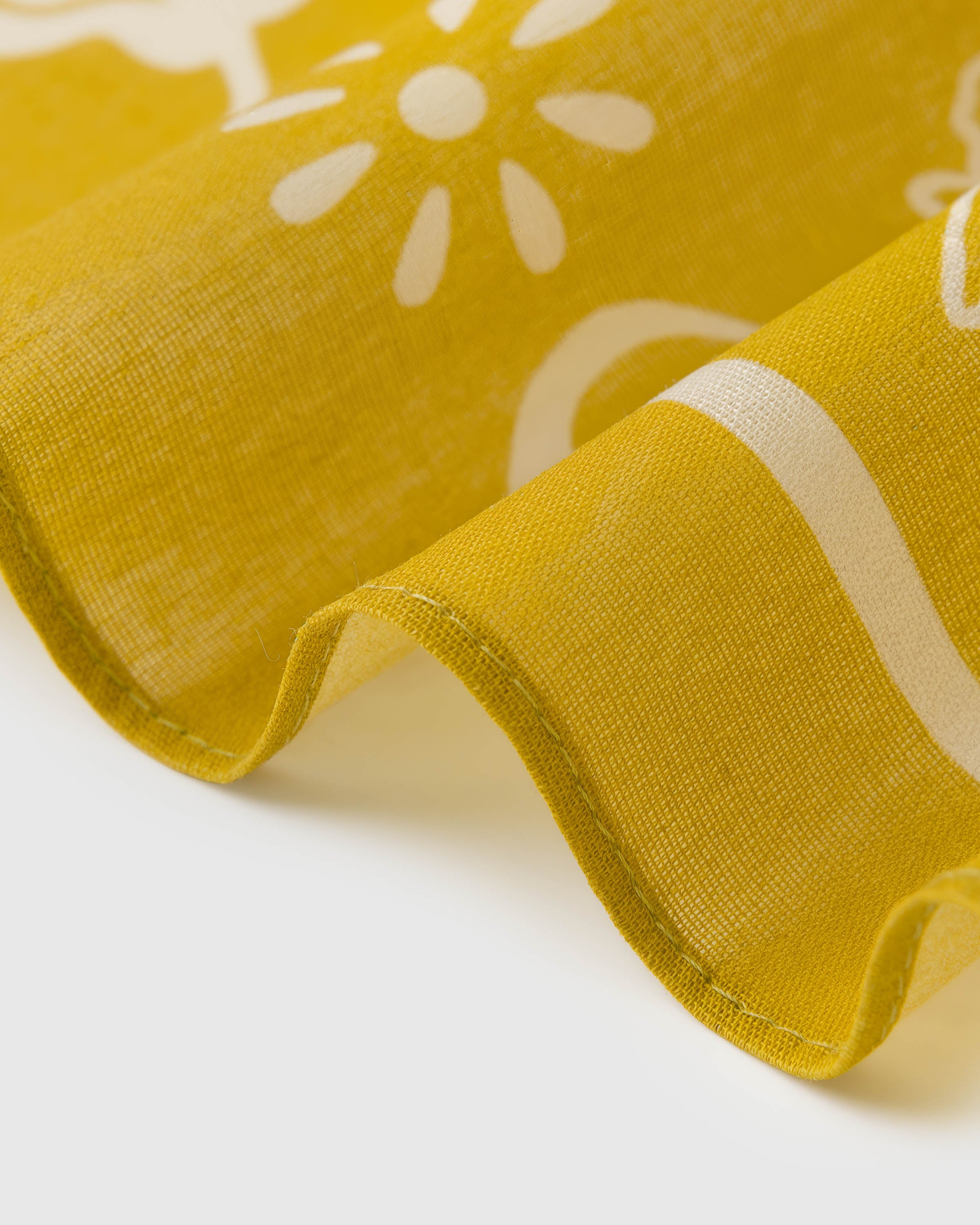 Close-up of the mustard silk scarf coiled to show the soft drape and ivory daisy silhouette