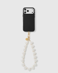 Black phone with the milky white heart bead wrist strap hanging in a soft loop, gold hook and disc at the top.