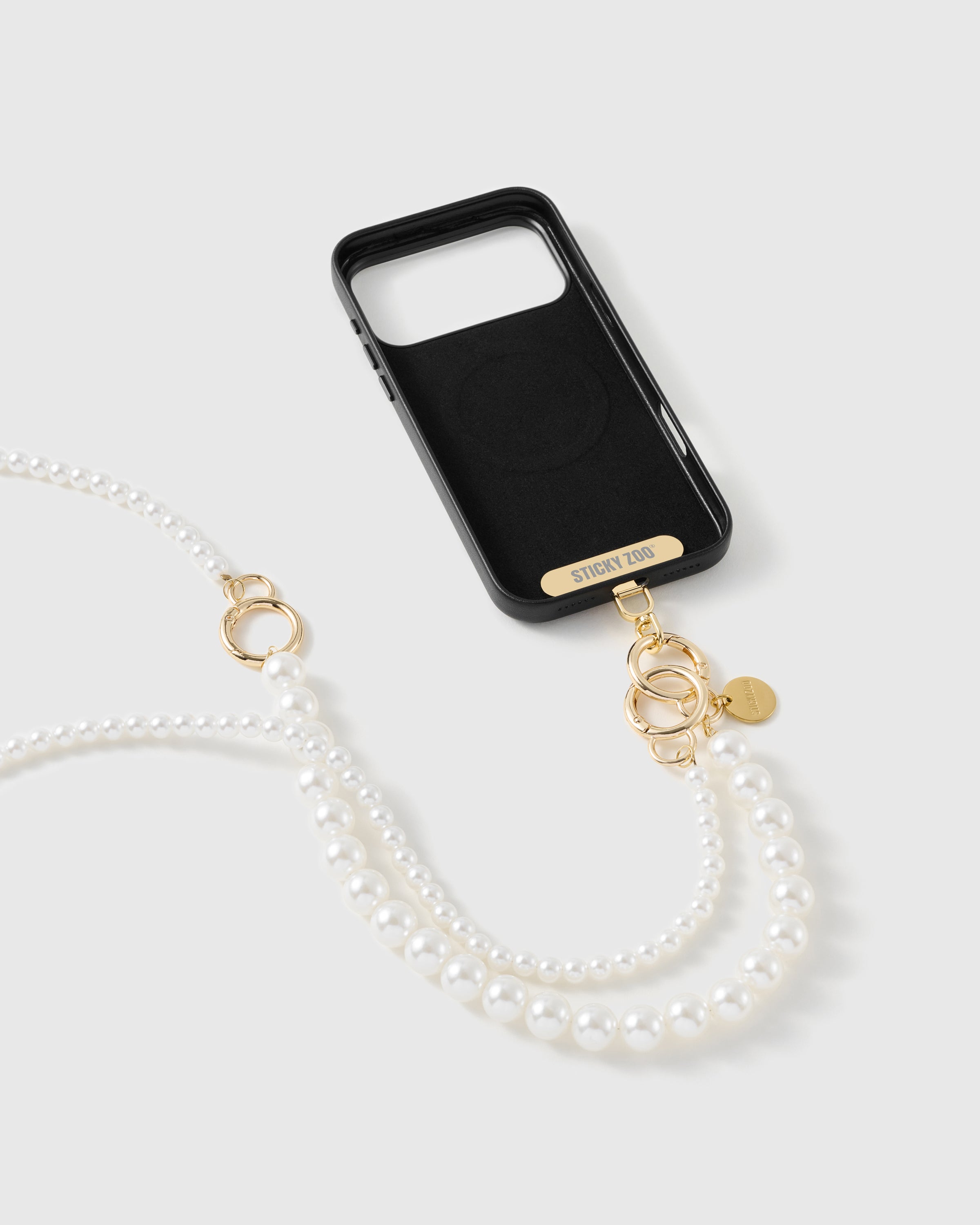 Black phone case with a gold-tone STICKYZOO plate and dual gold clasps holding the two-size faux-pearl strap