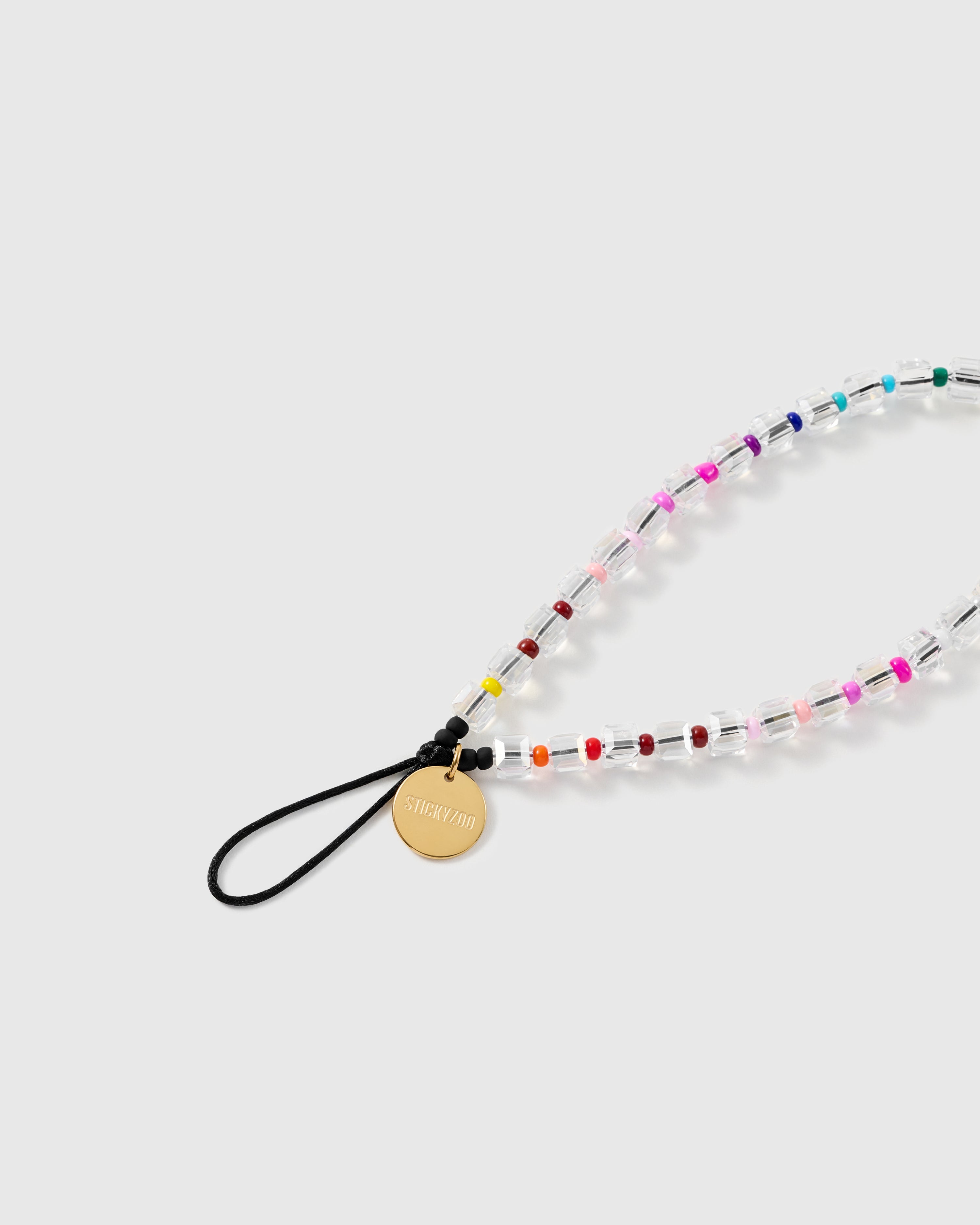 Close-up of the black stretch-cord loop and engraved gold-tone STICKYZOO disc beside clear faceted beads and colourful seed beads.