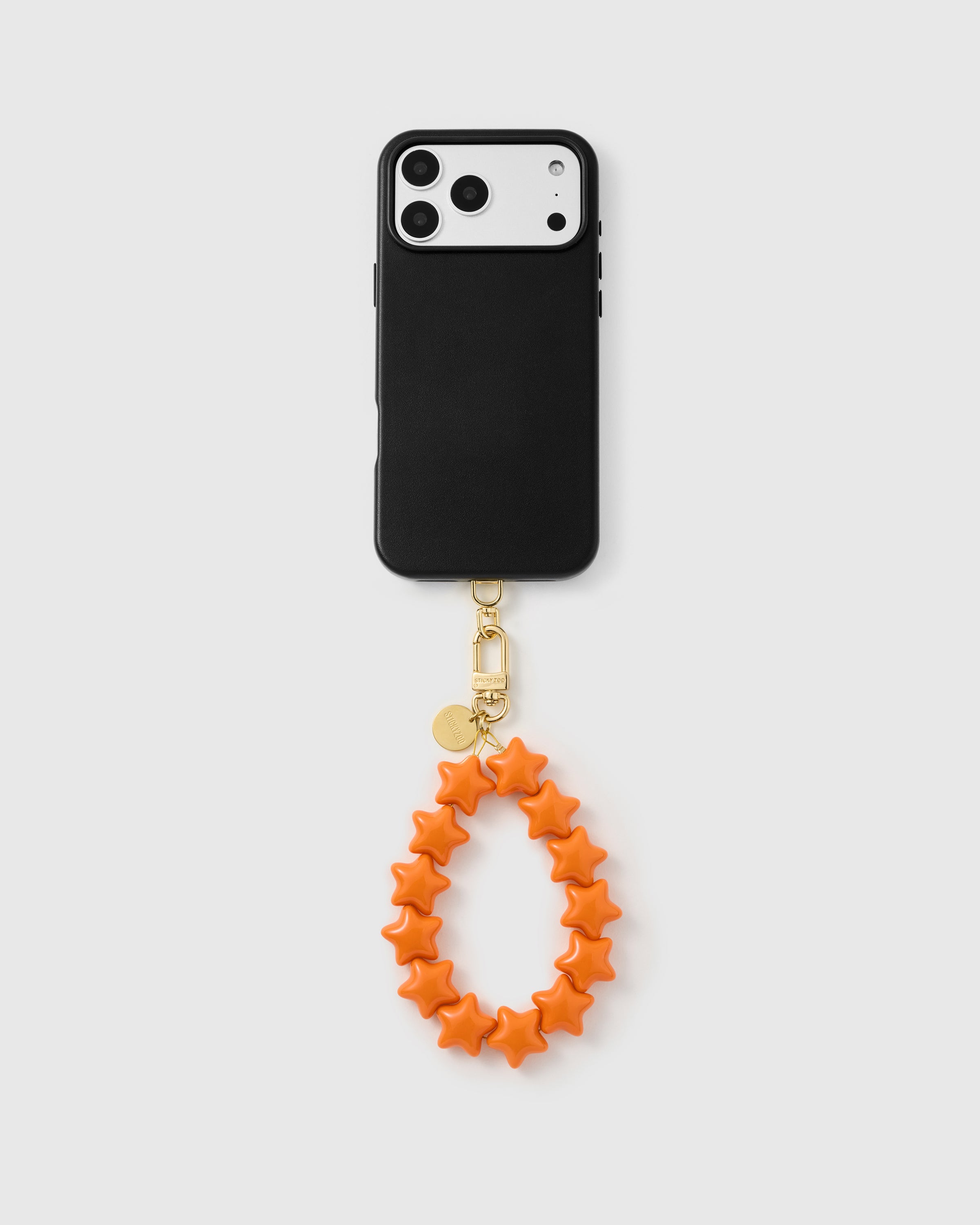 Full phone with the tangerine star strap clipped on, hanging from the base of a black phone case.