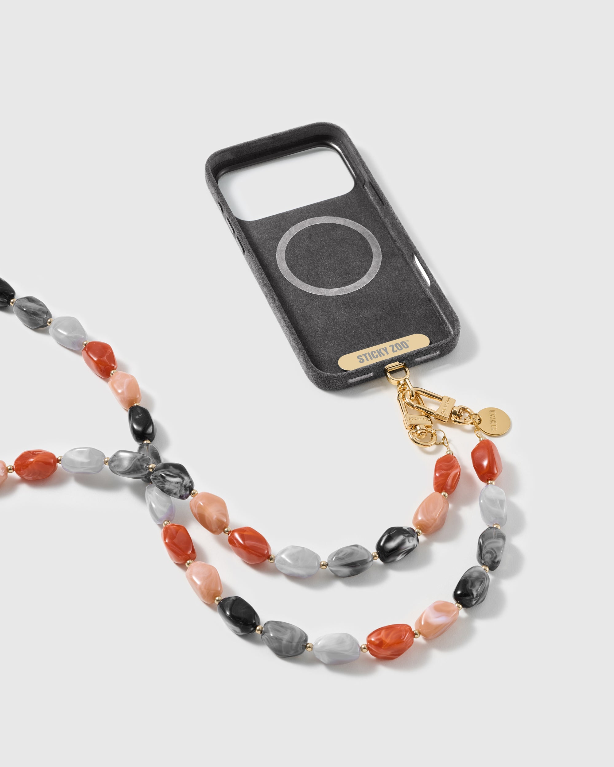Full phone wearing the long STICKYZOO strap, studio shot showing 18K gold-plated engraved hardware.