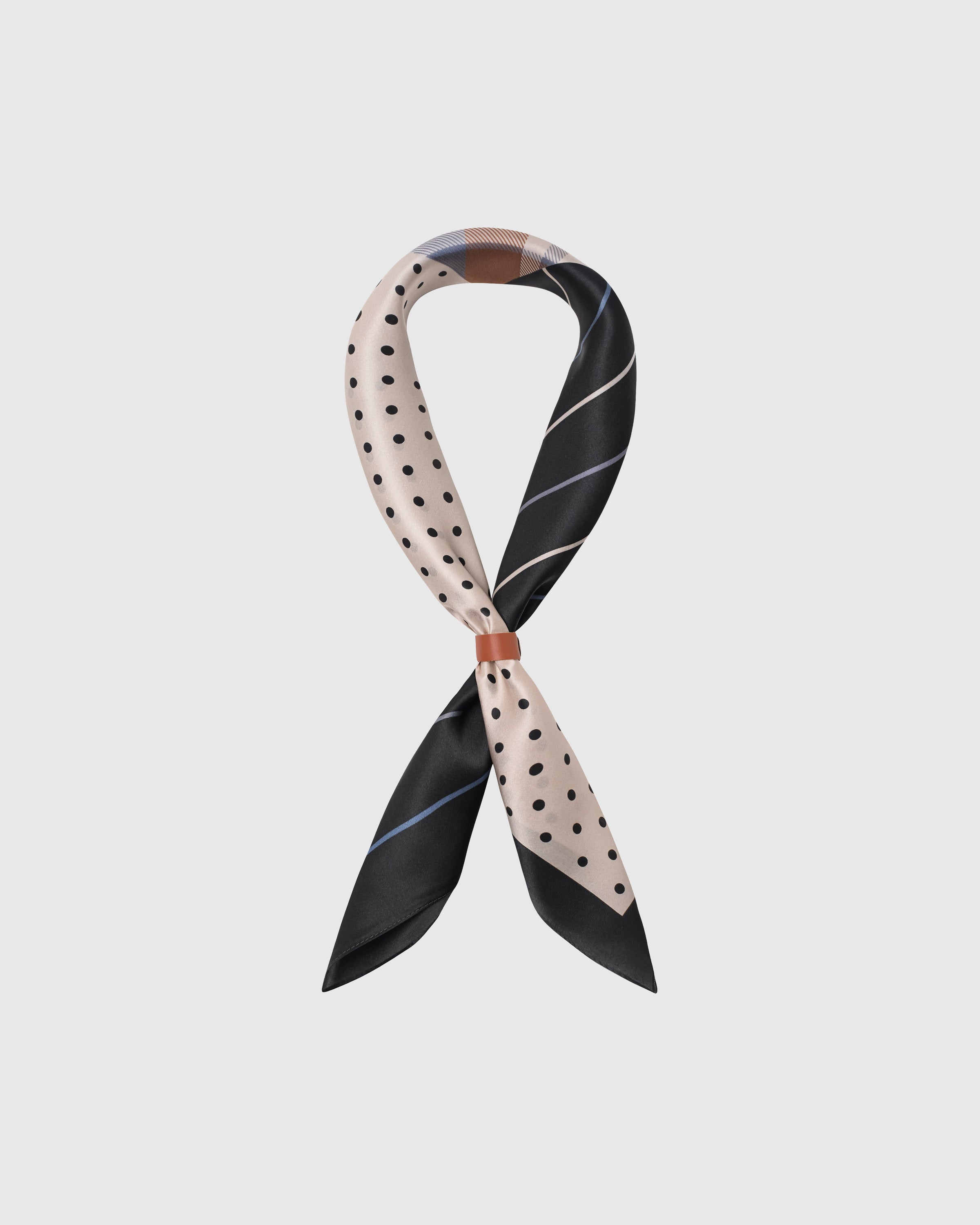 STICKYZOO patchwork silk scarf knotted through a leather slide showing polka, plaid and pinstripe quadrants