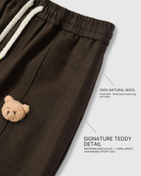Close-up of hand-stitched plush teddy bear face on dark brown wool-blend fabric showing dimensional texture