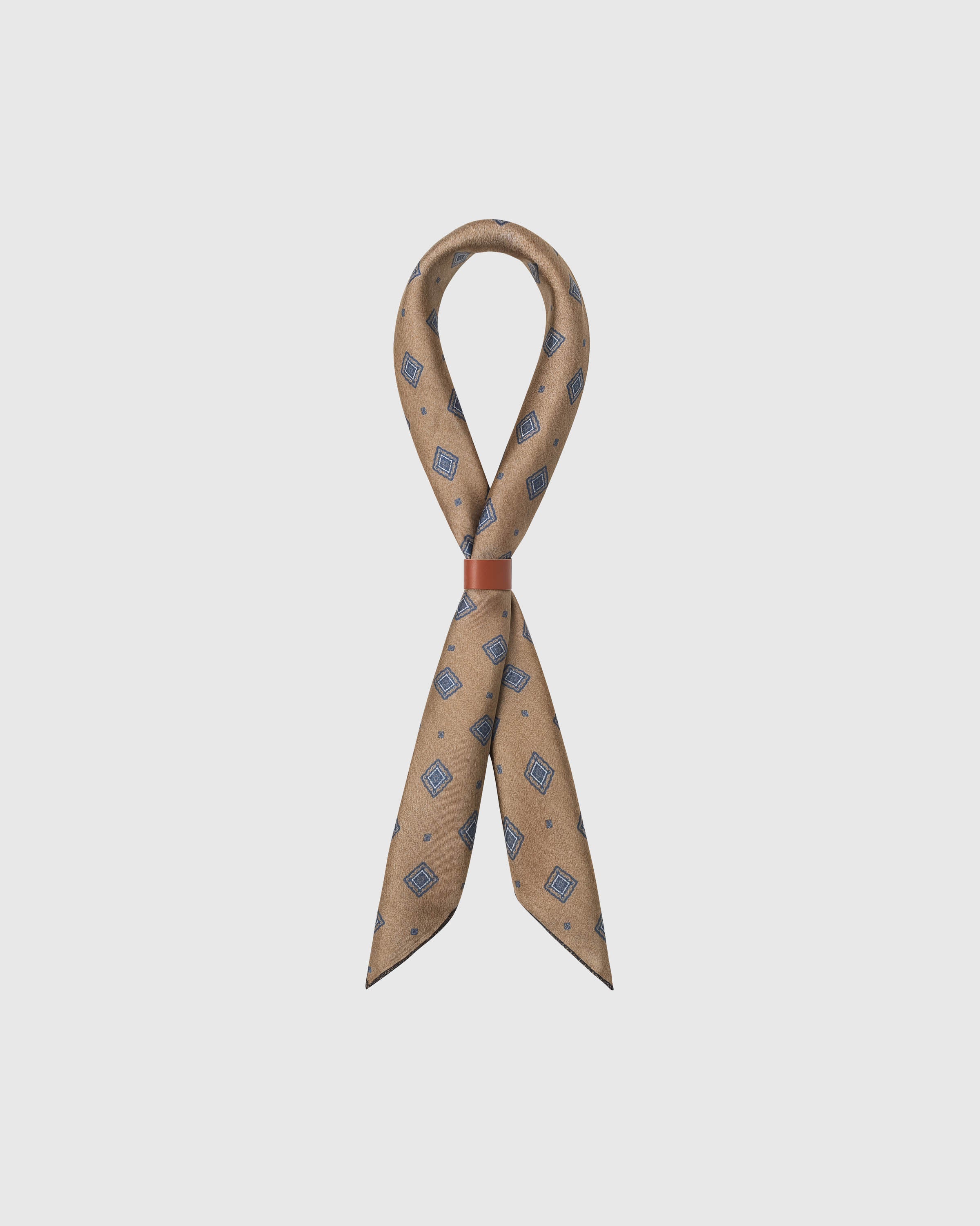 Camel silk foulard scarf draped in a ribbon fold with a slim leather slide showing the diamond medallion print