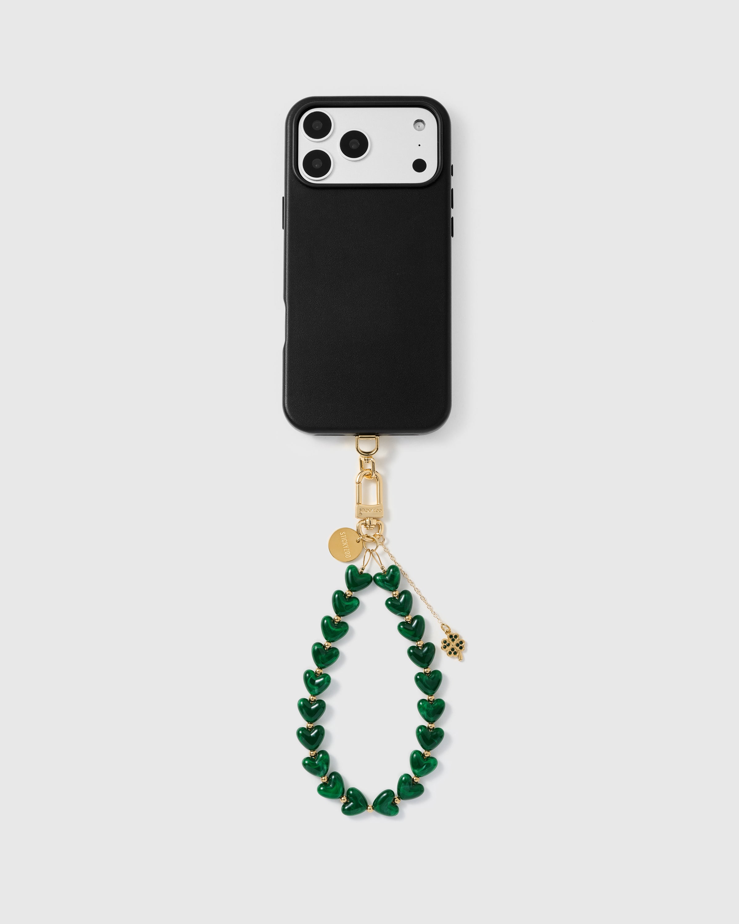 WORKS WITH ANY CASE — Full phone with emerald clover heart strap attached, gold clover charm centered — "People stop me to ask about it." Mia K.
