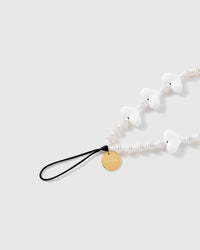 Close-up of the gold STICKYZOO disc and black stretch-cord loop beside glossy white heart beads and ribbed cream-white disc beads.
