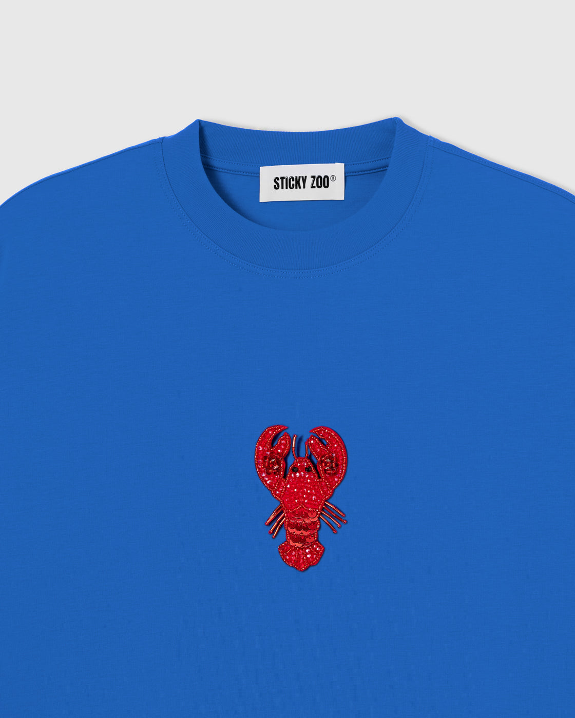 Hand-beaded lobster on the blue Lobster T-Shirt showing red glass beads and layered sequins on 230gsm cool-touch cotton.
