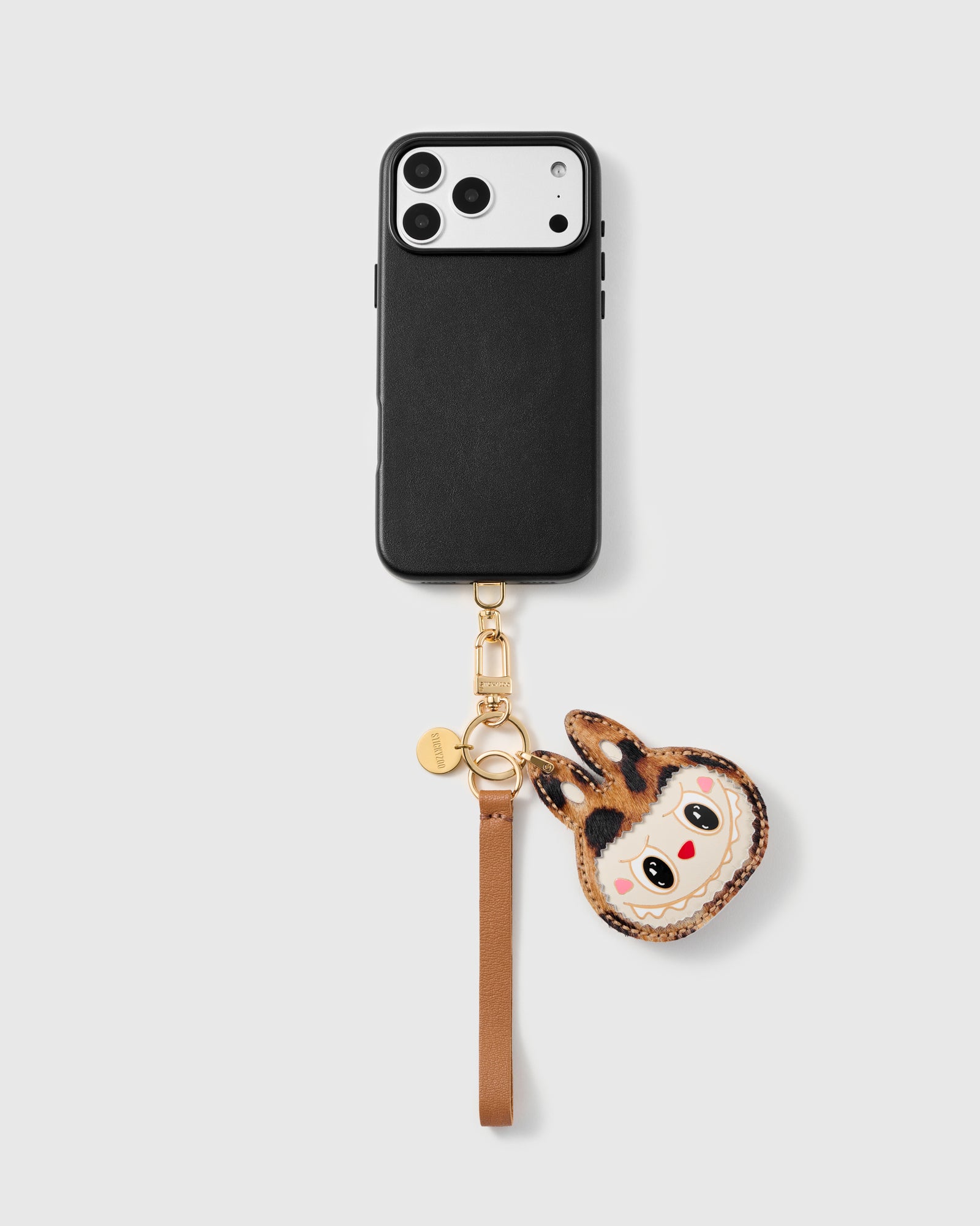 Leopard critter leather phone strap clipped to a black phone case, hands-free cognac wrist strap