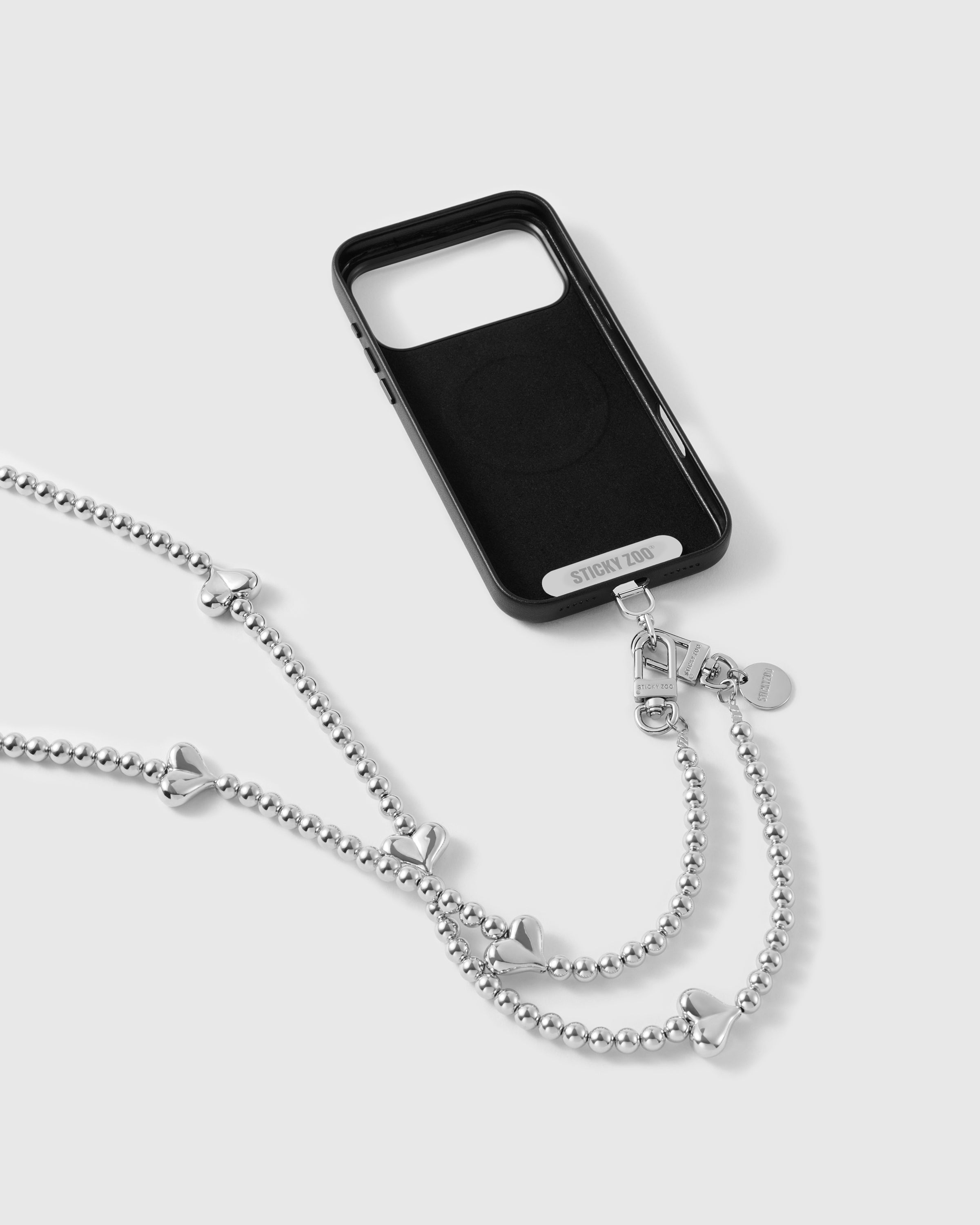 STICKYZOO silver-tone crossbody strap clipped to a black phone case with dual clasps, chain and puffy heart beads draping down.