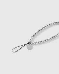 Close-up of the black stretch-cord loop knotted to an engraved silver-tone STICKYZOO disc beside smooth silver ball beads