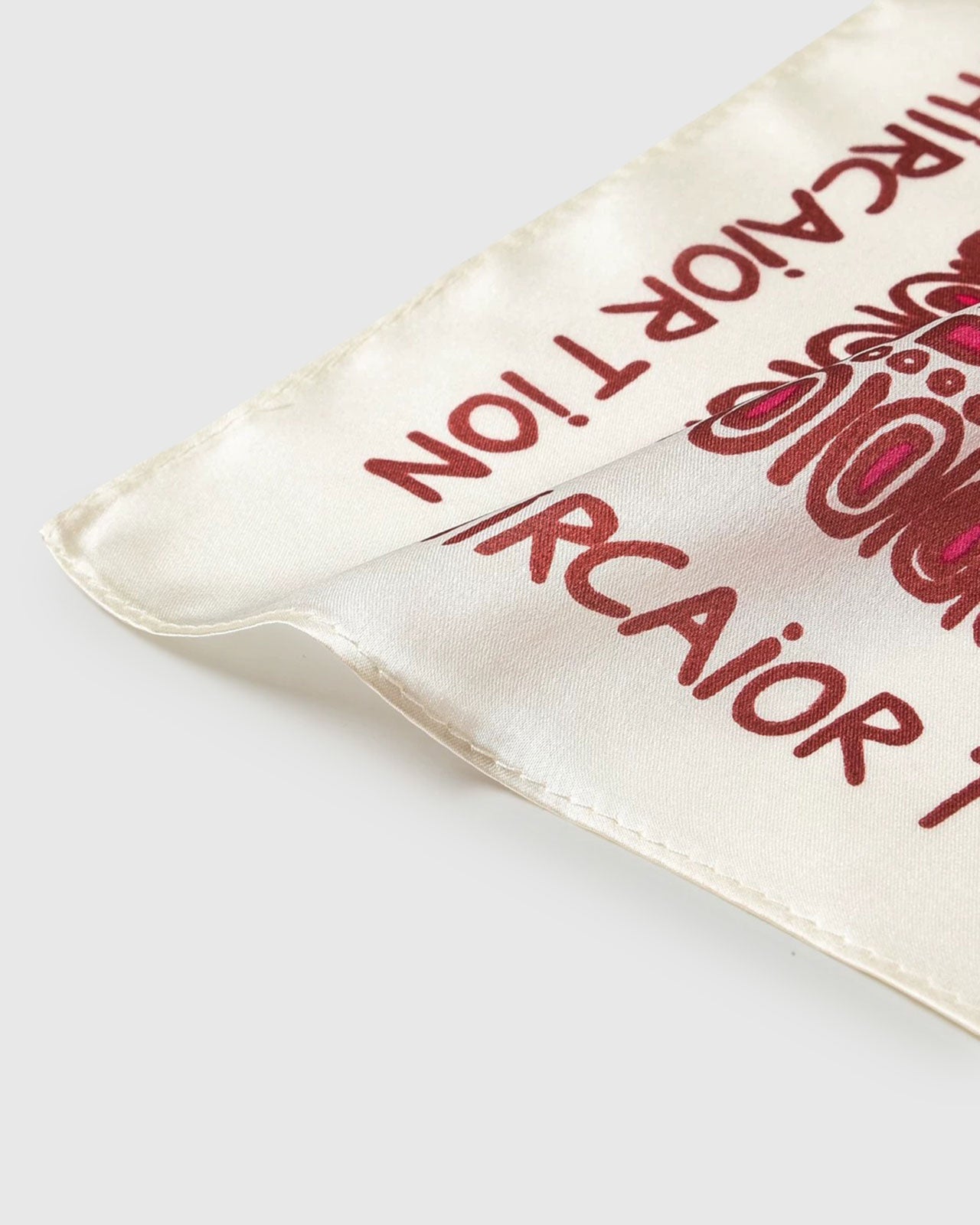 Close-up of the cream silk scarf showing the crimson lettered border and the soft fold of pure silk