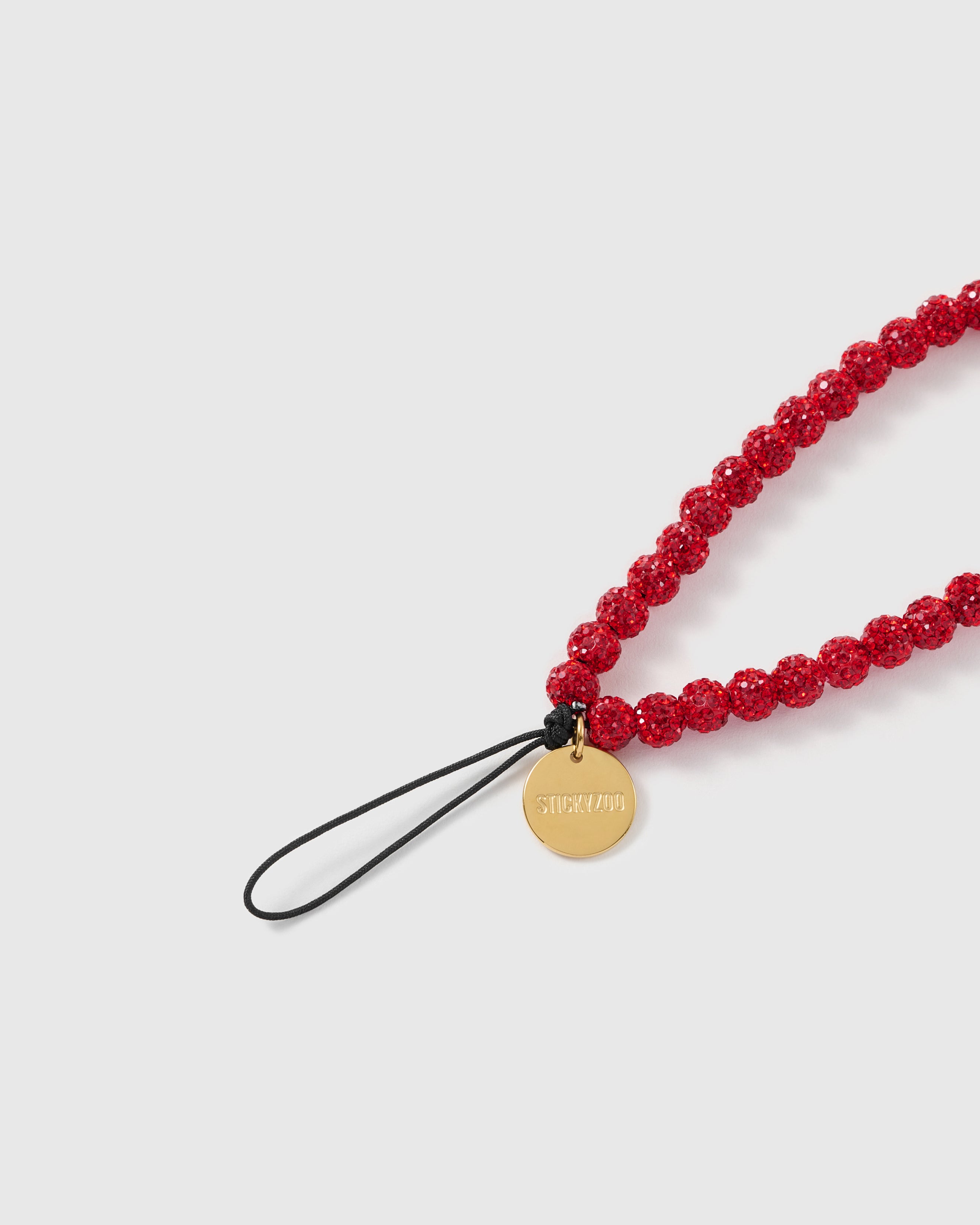 Close-up of ruby crystal-pave sparkle beads and the engraved STICKYZOO disc on a handmade phone strap