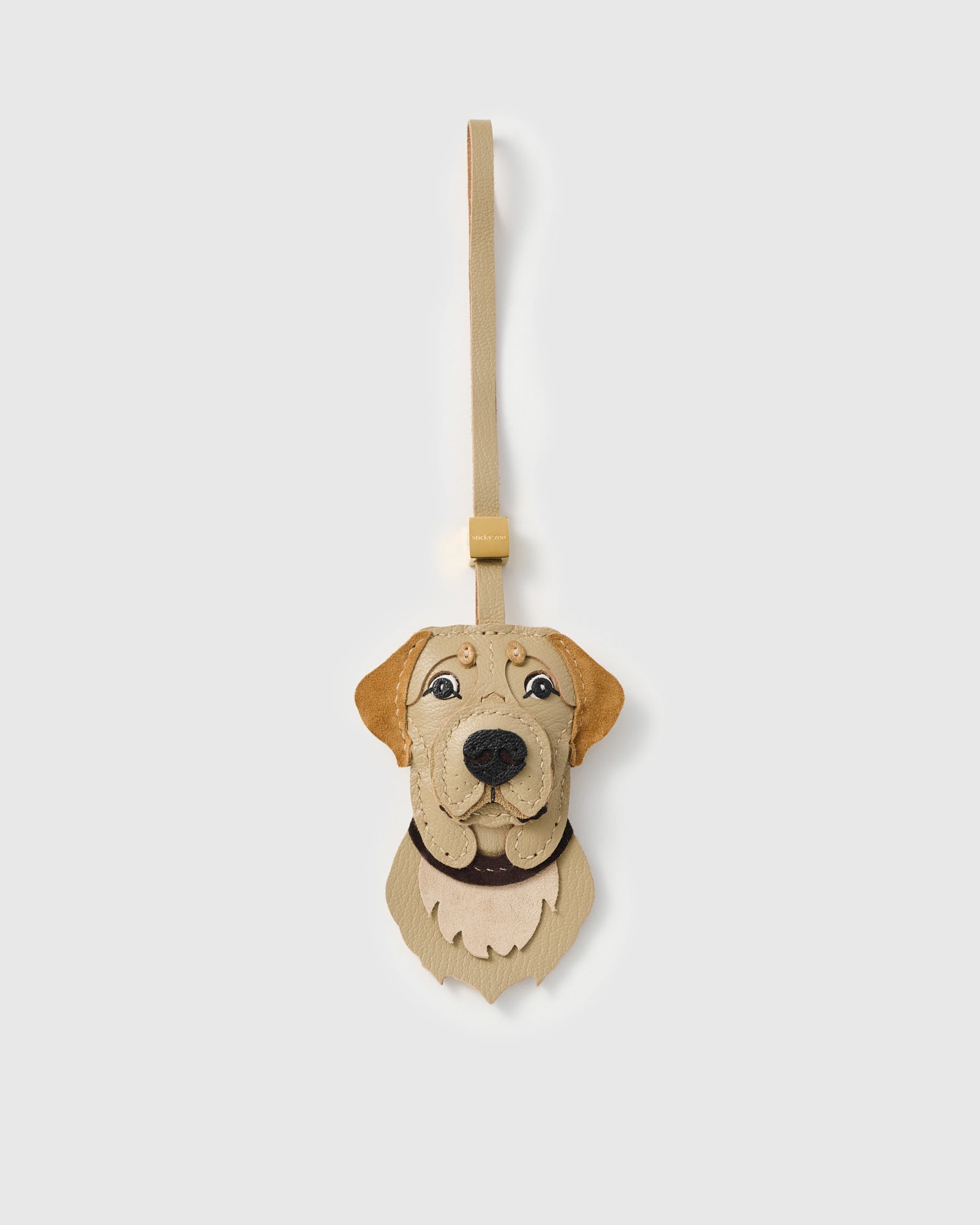 {{French leather + suede.}} English Labrador Retriever charm handmade from French Alran goatskin and French Alran suede — sand-champagne face, Labrador suede floppy ears, dark nose, feathered suede chest fur, champagne strap. Three days by hand. Arrives in luxury gift packaging. Designed in Amsterdam.
