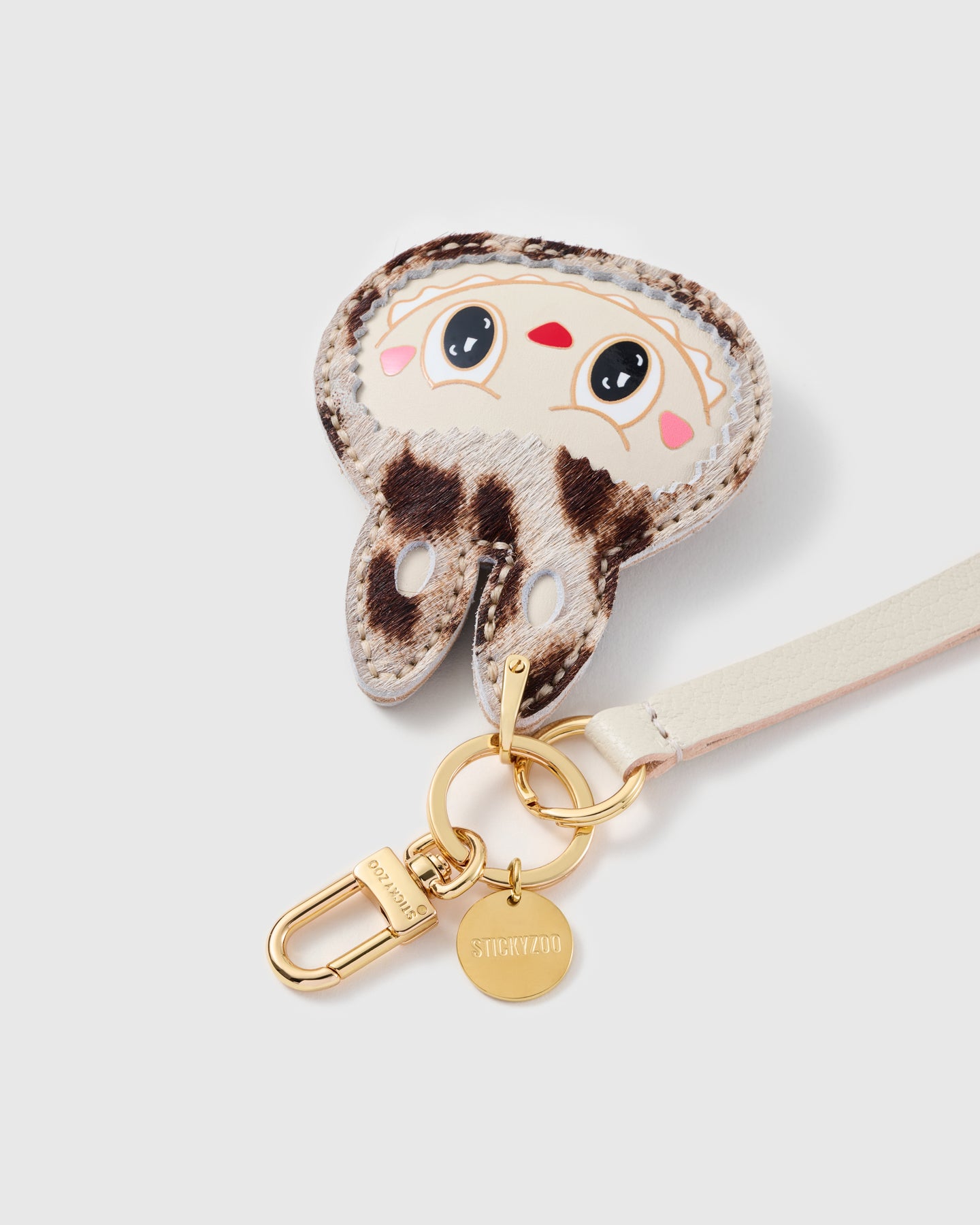 Snow-leopard leather phone strap close-up — calf-hair charm, hand whip-stitched edge, STICKYZOO engraved hook