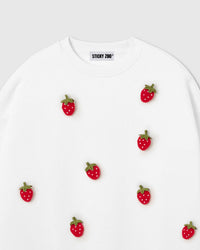 Close-up of plush strawberry with red body, white seed dots, and green stem on cream premium cotton