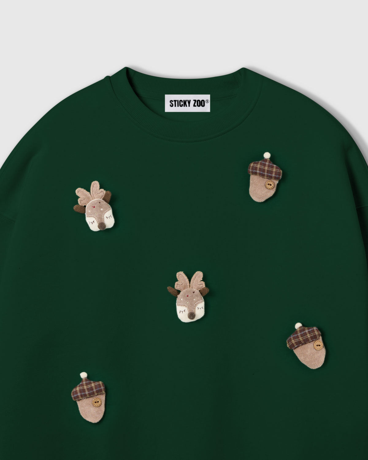 {{Not printed — stitched}} Close-up of plush reindeer face with felt antlers on forest green cotton showing 3D dimensional depth