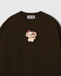 Close-up of hand-stitched plush puppy applique on brown cotton showing cream sherpa body, brown eye patch, and layered 3D texture