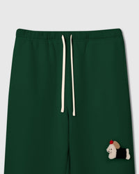 Close-up of hand-stitched plush dachshund with black coat and red apple on forest green 350gsm cotton sweatpants