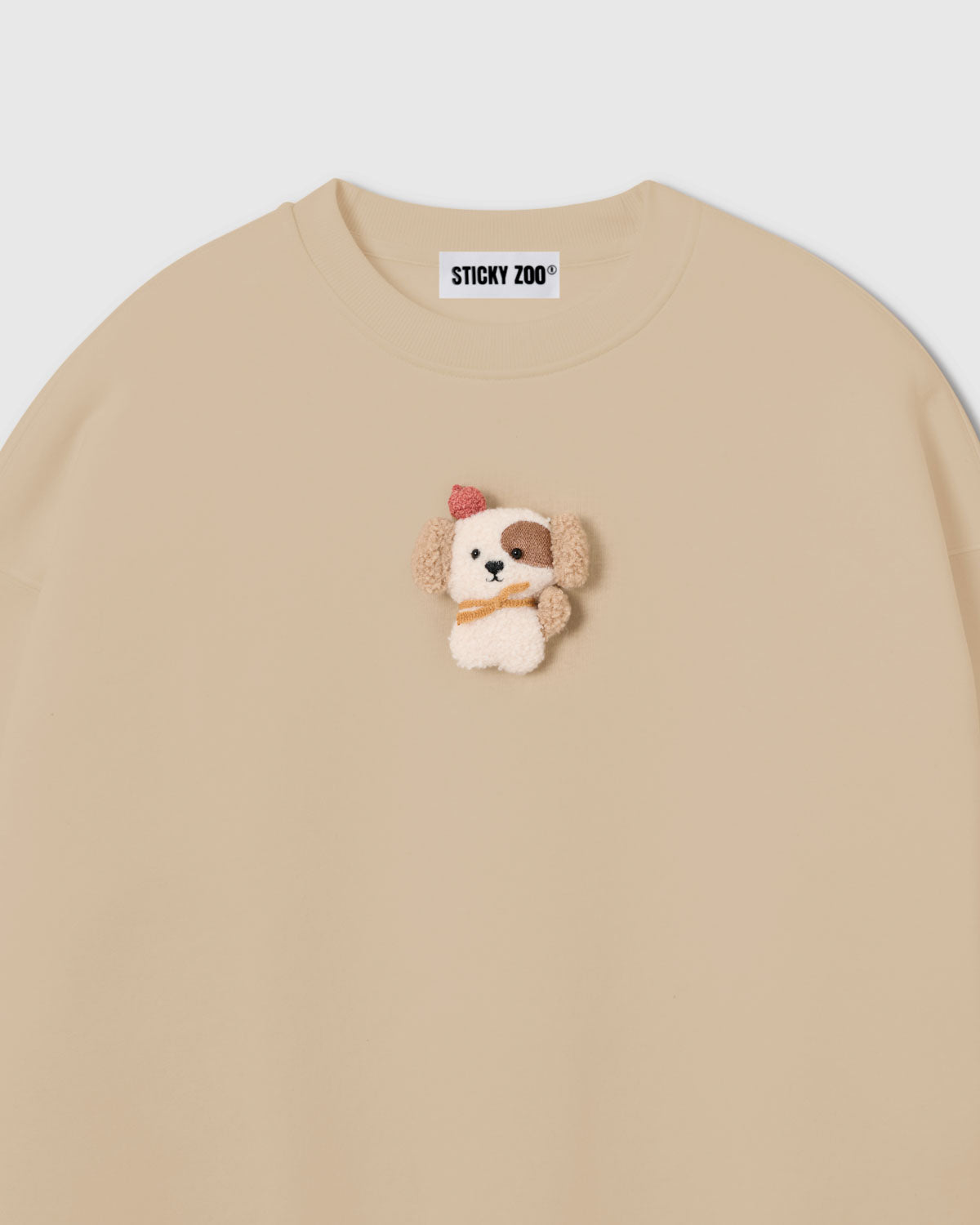 {{Not printed — stitched}} Close-up of plush puppy applique on cream cotton showing sherpa texture, red beret, golden scarf, and embroidered detail