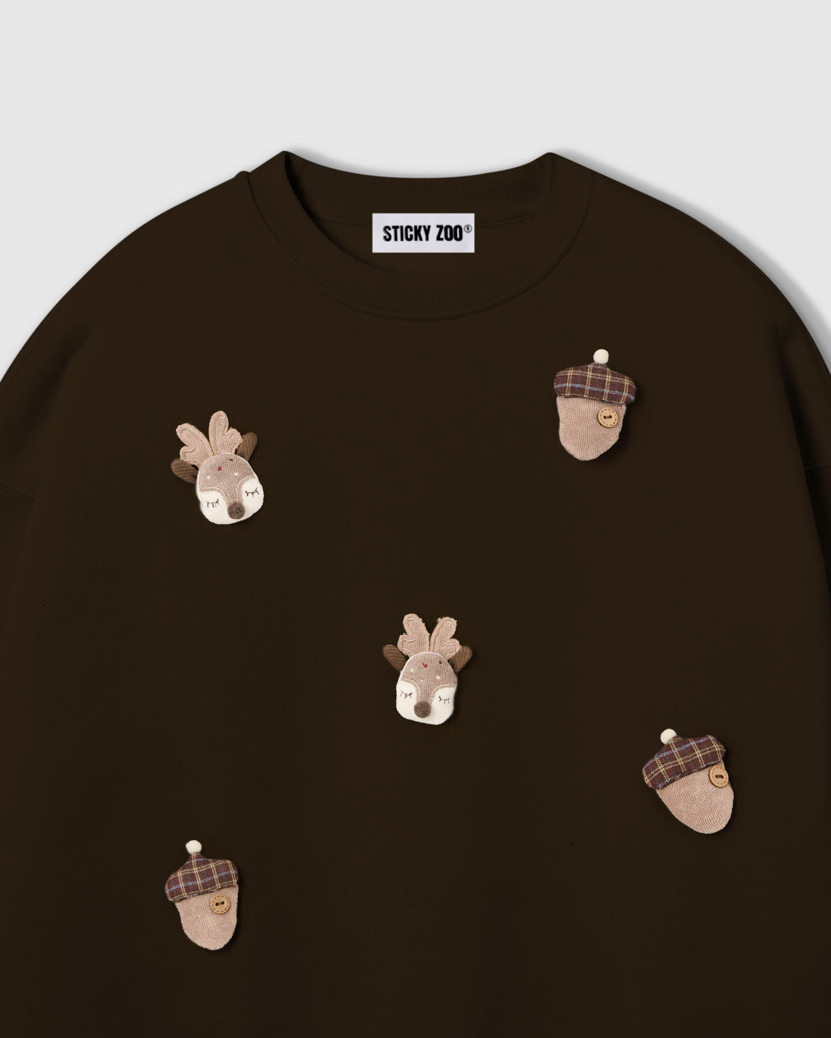 {{Not printed — stitched}} Close-up of plush reindeer face with felt antlers and tartan acorn on dark brown cotton