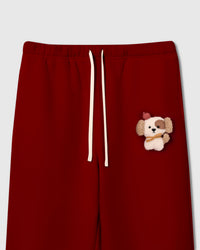 Close-up of plush puppy on red cotton fleece showing sherpa texture, red beret, golden scarf, and embroidered detail