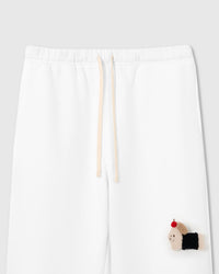 Close-up of hand-stitched plush dachshund with black coat and red apple on white 350gsm cotton sweatpants showing dimensional texture