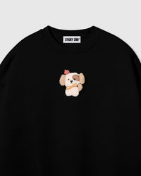 Close-up of hand-stitched plush puppy on black cotton showing cream sherpa body, pink beret, and golden scarf