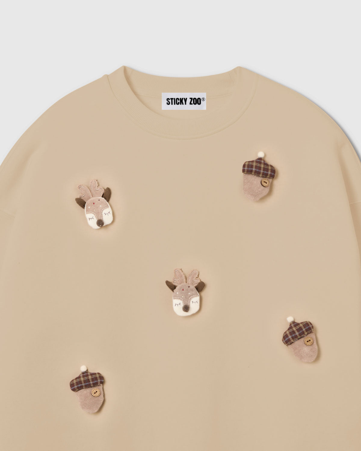 {{Not printed — stitched}} Close-up of hand-stitched plush reindeer face with felt antlers and embroidered features on cream cotton