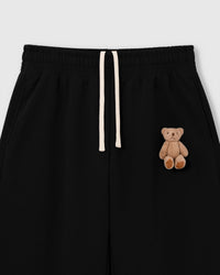 Close-up of hand-stitched 3D plush teddy bear on black 450gsm cotton fleece showing dimensional texture